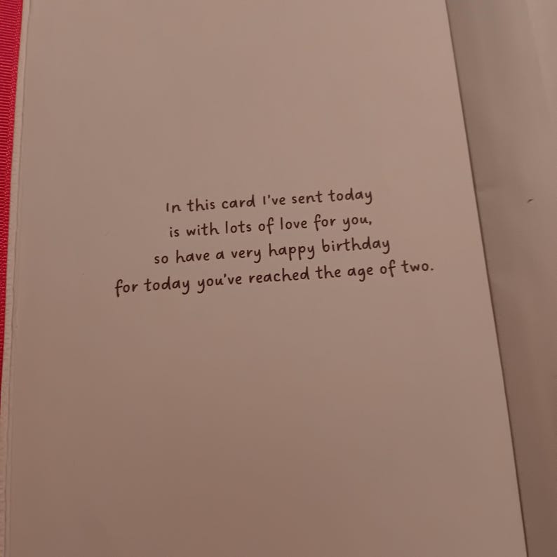 May include: A white birthday greeting card with a pink edge featuring the black printed text: In this card I've sent today is with lots of love for you, so have a very happy birthday for today you've reached the age of two.