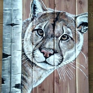 May include: A painting of a cougar's face peeking out from behind a wooden plank. The cougar has brown fur, green eyes, and a pink nose. The wooden plank has a light brown color and a vertical grain pattern.