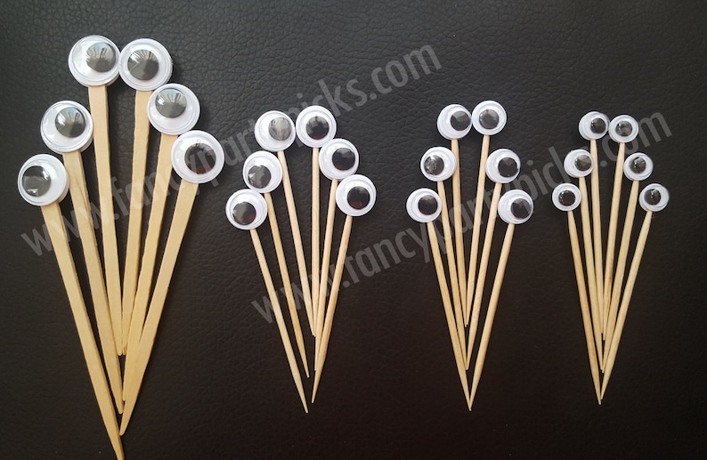 May include: Assortment of googly eyes on wooden skewers, in various sizes. The eyes are white with black pupils and are arranged in groups of different sizes.