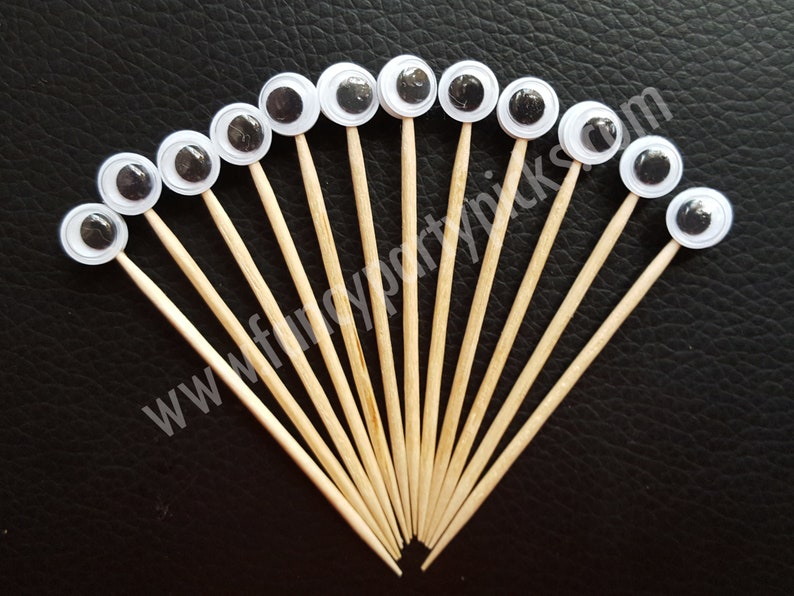 May include: A set of 15 white googly eyes on wooden skewers. The eyes are black and white and are arranged in a fan shape.