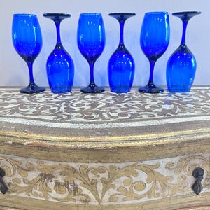 May include: A set of six cobalt blue glass wine glasses arranged in a row. Three glasses are standing upright on their circular bases, while the other three are inverted, resting on their rims to display the stems and bowls.