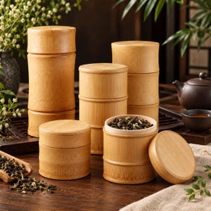 Puede incluir: Una colección de recipientes de almacenamiento cilíndricos de bambú con tapas a juego. Los recipientes presentan una textura natural de grano de madera marrón claro y están dispuestos a varias alturas. Un recipiente abierto muestra té.