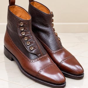 Peut inclure: Une paire de bottines bicolores avec des bouts en cuir marron lisse et des tiges en cuir grainé marron foncé. Les bottines présentent une fermeture latérale à six petits boutons marron, une languette au talon et une semelle foncée.