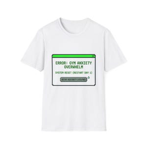 May include: A white short-sleeve t-shirt featuring a pixelated computer error window graphic in green, black, and gray. The text reads: ERROR: GYM ANXIETY OVERWHELM, SYSTEM RESET (RESTART DAY 1), and a button labeled RETRY RESTART? (YES/NO).