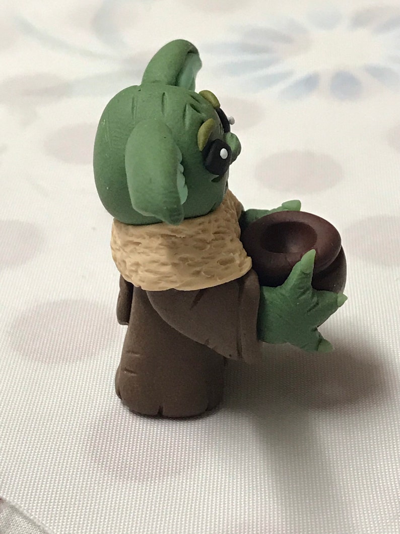 May include: A green and brown hand-crafted figurine of a popular character from the Star Wars franchise. The character is holding a brown bowl in its hand.