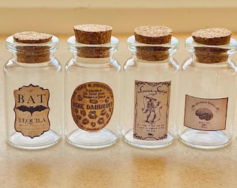 May include: Six small glass bottles with cork stoppers and labels. The labels have various Halloween-themed designs and text, including "Ghost Farts", "Bat Tequila", "More Dahbour", "Sauce Special", "The Spotted Brown", and "Mushroom Magic".