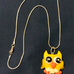 May include: A yellow owl charm necklace with black eyes and a pink beak. The owl is sitting on a silver chain.