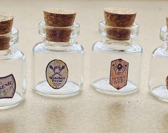 Op de afbeelding: Vier kleine glazen flesjes met kurkstoppen en etiketten. De etiketten lezen "Arsenic", "Witches Brew", "Spider Web" en "Toadflax".