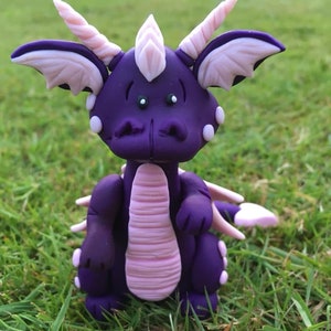 May include: A purple and pink dragon figurine with a friendly expression. The dragon has large wings, a long tail, and a spiky crest.