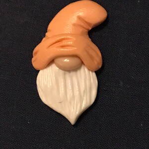 Puede incluir: Una pequeña figura de gnomo de color melocotón con barba blanca y un gorro bajado sobre los ojos.