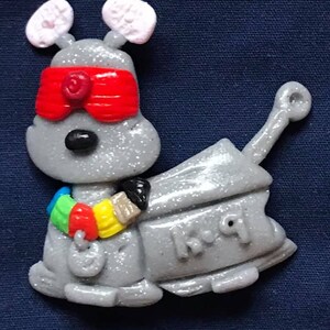 Peut inclure: Un jouet robot gris et paillet&eacute; avec des yeux rouges, des oreilles blanches et un bandeau color&eacute; autour du bras. Le robot tient un pinceau et porte l'inscription "K.I.Q" sur le c&ocirc;t&eacute;.