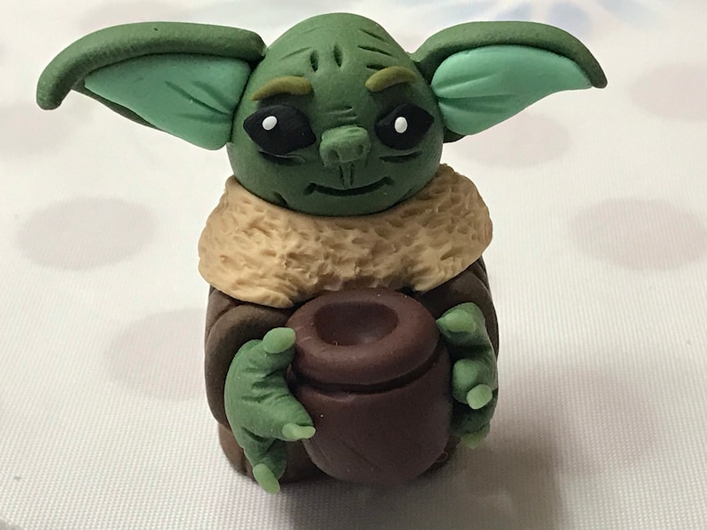May include: A green and brown handmade figurine of a character from the Star Wars franchise, holding a brown pot in its hands.