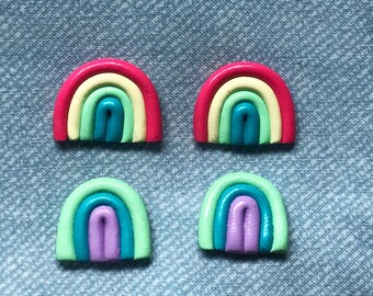 Op de afbeelding: Vier regenboogkleurige kleioorbellen. Elke oorbel is gevormd als een regenboog met vijf verschillende gekleurde strepen. De kleuren zijn rood, geel, groen, blauw en paars.