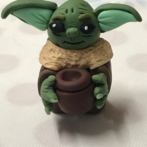 May include: A green and brown handmade figurine of a character from the Star Wars franchise, holding a brown pot in its hands.