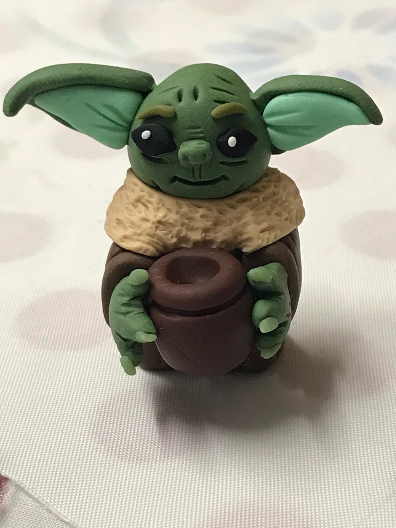 May include: A green and brown handmade figurine of a character from the Star Wars franchise, holding a brown pot in its hands.