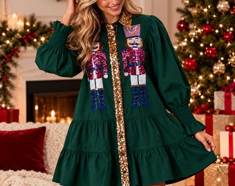 Könnte beinhalten: Ein dunkelgrünes Langarmkleid mit einer goldfarbenen Paillettenknopfleiste und einem Kragen. Das Kleid ist mit zwei großen, bunten Pailletten-Nussknackerfiguren auf der Vorderseite verziert und hat einen gestuften Rock mit Bündchen.