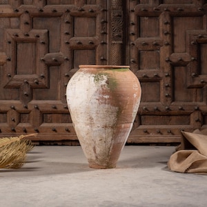 May include: A large, tapered terracotta vessel featuring a weathered, uneven white wash finish with visible patches of green moss-like discoloration. The jar has a wide, circular opening and a narrow base, showcasing a textured, aged surface.