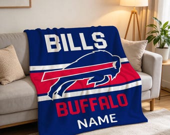 Może przedstawiać: Niebieski koc z polaru z białym napisem BILLS u góry, dużym czerwono-białym logo Buffalo Bills pośrodku oraz czerwonym napisem BUFFALO, po którym następuje biały napis NAME u dołu wzoru znajdującego się na kocyku.