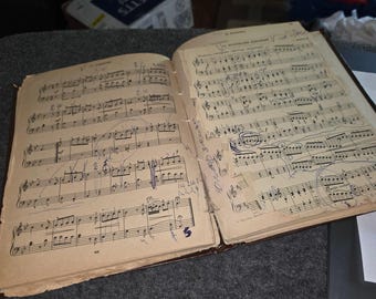 May include: An open vintage music book with aged, yellowed pages featuring printed musical notation. The score is heavily annotated with handwritten pencil and blue ink markings, including circles, lines, and numbers throughout the staves.