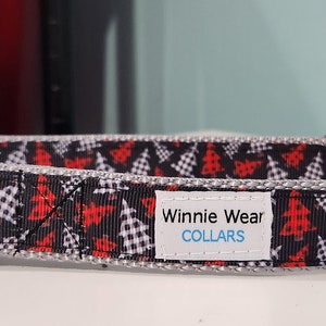 May include: A black and white dog collar with a red and white checkered Christmas tree pattern. The collar has a silver D-ring and a black buckle. The collar has a white label that says "Winnie Wear COLLARS".