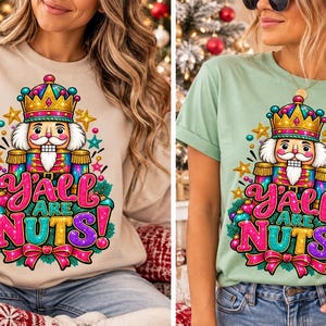 Puede incluir: Una sudadera beige y una camiseta verde claro, cada una con un gráfico colorido de un cascanueces con corona, rodeado de estrellas y adornos, con el texto Y'ALL ARE NUTS! en letras brillantes de color rosa, azul y amarillo.