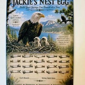 May include: A rectangular metal sign titled Jackie's Nest Egg featuring a bald eagle with two chicks in a nest. The background shows a lake and mountains. Below the nest are twenty illustrated branches for tracking savings with text labels.