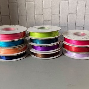 May include: Eight spools of satin ribbon in various colors, including hot pink, turquoise, orange, navy blue, lime green, purple, red, and lavender. The spools are arranged in two rows of four.
