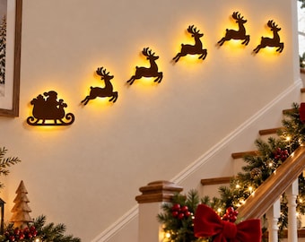 May include: A set of dark brown wall-mounted silhouettes featuring Santa in a sleigh followed by five flying reindeer. Each piece is backlit with a warm yellow glow, creating a festive display arranged in an upward diagonal line on the wall.