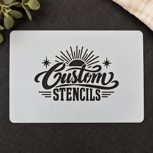 Puede incluir: Una plantilla rectangular blanca con un diseño gráfico negro que incluye un icono de sol, estrellas de cuatro puntas y el texto Custom STENCILS en una combinación de letra cursiva y negrita con líneas horizontales.