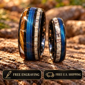 May include: Two rings featuring a black band with a central blue pinstripe inlay. The wider ring includes segments of brown wood and textured white antler, while the narrower ring features a textured white antler inlay alongside the blue stripe.