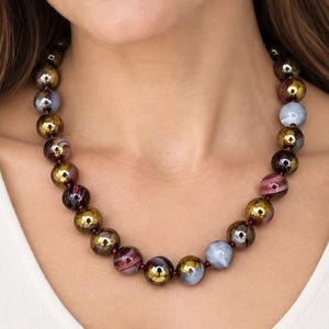 May include: A beaded necklace featuring a repeating pattern of spherical beads in metallic gold, translucent light blue, and deep burgundy with swirling marbled textures. The beads are strung together on a thin cord, creating a circular collar design.