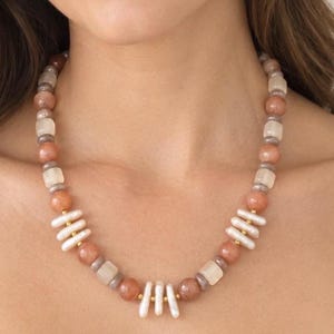 The Soleil necklace worn at the collarbone: peach moonstone beads alternating with clusters of white freshwater pearls and small gold-colored accents.