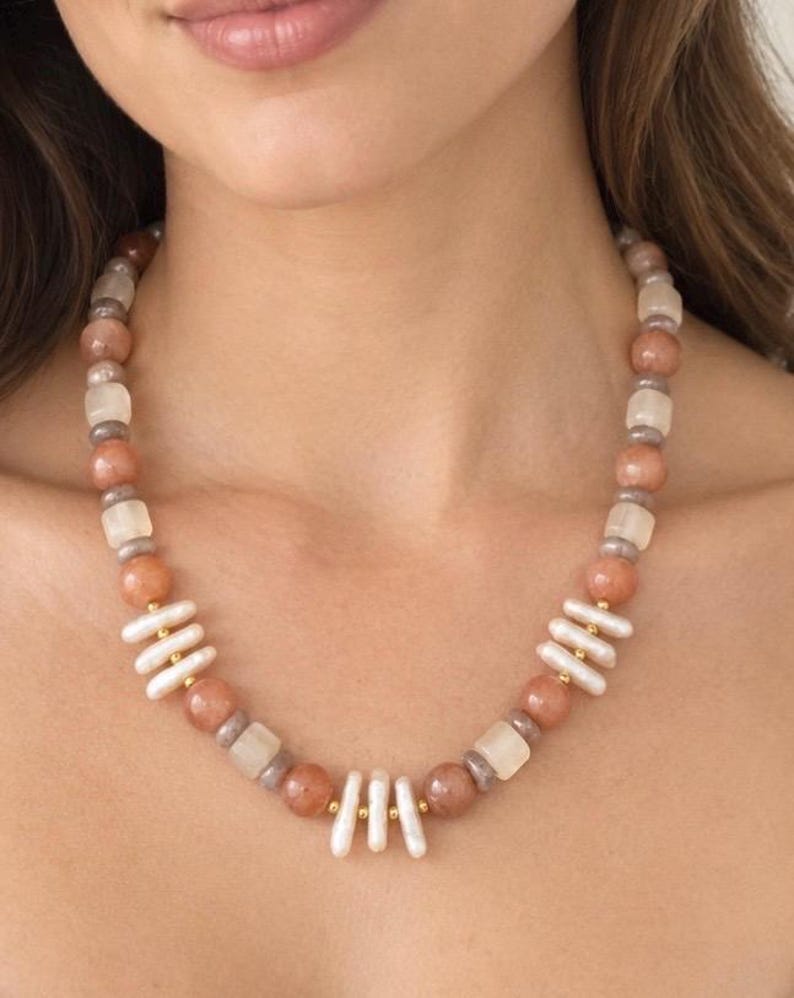 The Soleil necklace worn at the collarbone: peach moonstone beads alternating with clusters of white freshwater pearls and small gold-colored accents.