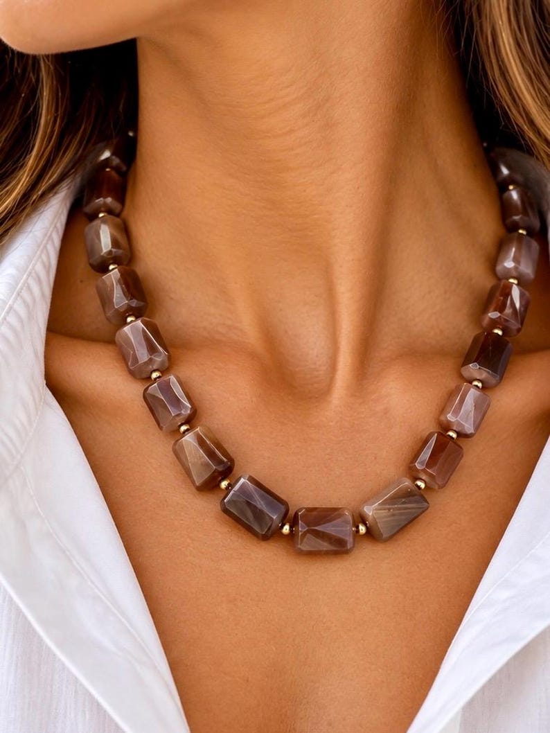 The Delphine necklace worn with an open white shirt: faceted chocolate moonstone beads in brown and taupe, separated by small gold-filled accents.