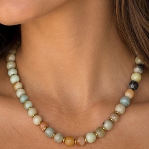 The Carmel necklace worn at the collarbone: round amazonite beads in pale green, tan and gray tones with small gold-colored spacers.