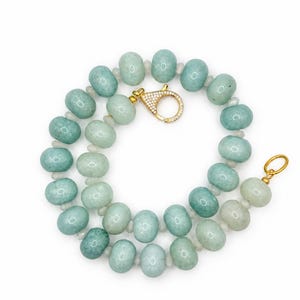 May include: A necklace composed of round, light green, semi-translucent beads separated by small, clear spacers. The piece features a gold-toned circular clasp encrusted with small, clear stones and a plain gold-toned circular ring at the other end.