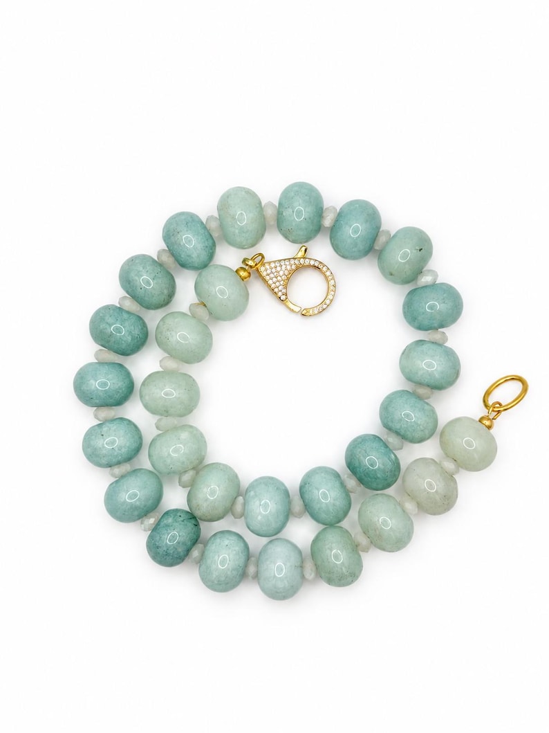 May include: A necklace composed of round, light green, semi-translucent beads separated by small, clear spacers. The piece features a gold-toned circular clasp encrusted with small, clear stones and a plain gold-toned circular ring at the other end.