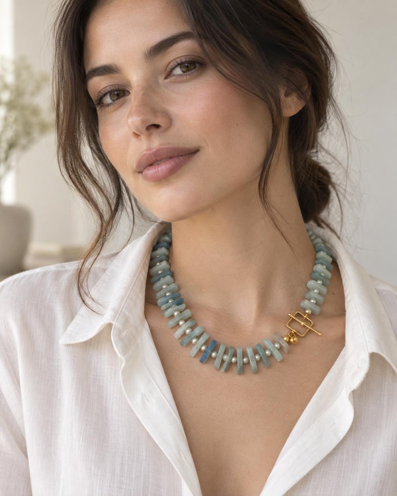 Peut inclure: Un collier compos&eacute; d'une alternance de perles rectangulaires en pierre bleu clair et de petites perles sph&eacute;riques blanches. Le bijou est ferm&eacute; par un fermoir &agrave; bascule en m&eacute;tal dor&eacute;, form&eacute; d'un cadre carr&eacute; et d'une barre en T &agrave; l'avant.