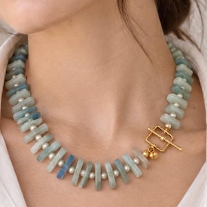 The St. Tropez necklace worn with a white shirt: pale blue aquamarine beads and white freshwater pearls with a gold-colored toggle clasp at the front.
