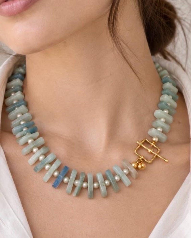 The St. Tropez necklace worn with a white shirt: pale blue aquamarine beads and white freshwater pearls with a gold-colored toggle clasp at the front.