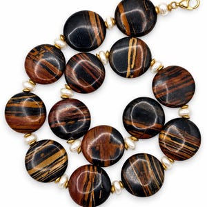 The Sutton necklace laid in a loose curve on white, with large round black, brown and rust-striped beads, creamy pearls, gold-tone spacers and a gold-tone clasp.