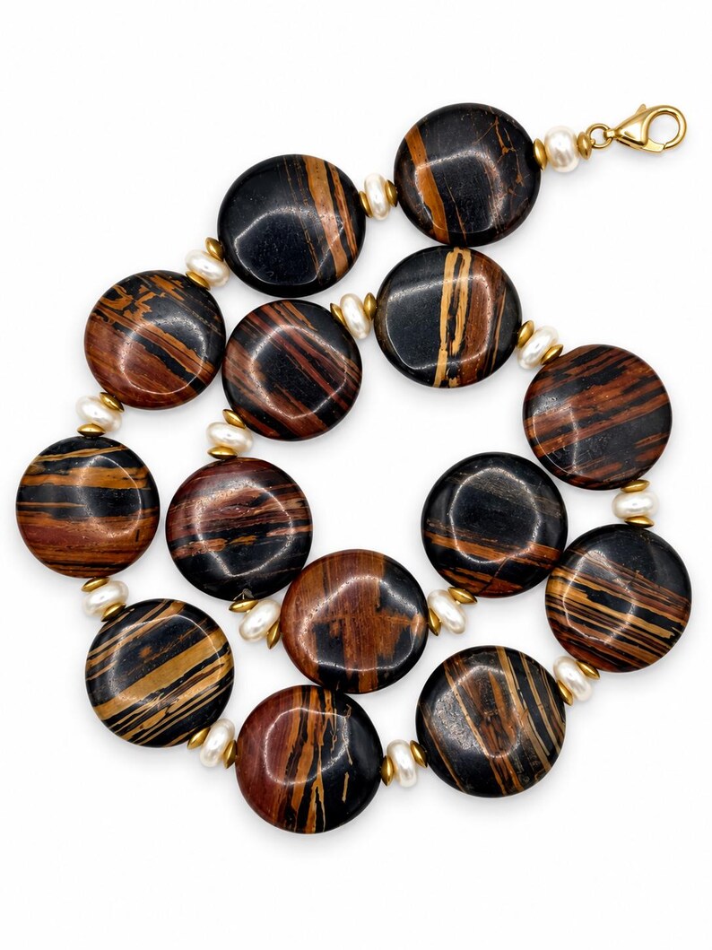 The Sutton necklace laid in a loose curve on white, with large round black, brown and rust-striped beads, creamy pearls, gold-tone spacers and a gold-tone clasp.