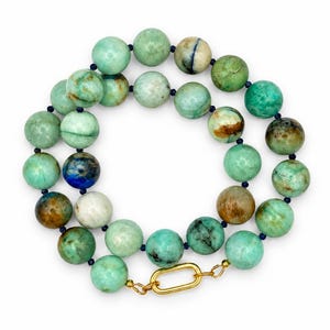 The Amalfi necklace coiled on a white background: round chrysocolla beads in green, aqua and brown, small dark blue lapis lazuli accents and a gold-tone clasp.