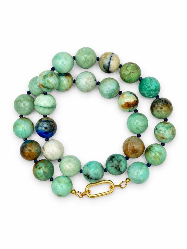 The Amalfi necklace coiled on a white background: round chrysocolla beads in green, aqua and brown, small dark blue lapis lazuli accents and a gold-tone clasp.
