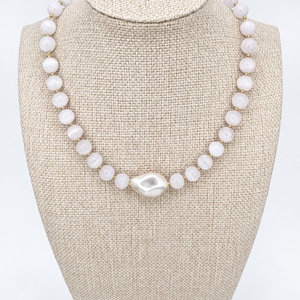 The Margaux necklace on a beige linen display bust: round pale pink gemstone beads with small gold-filled spacers and a white baroque pearl centerpiece.