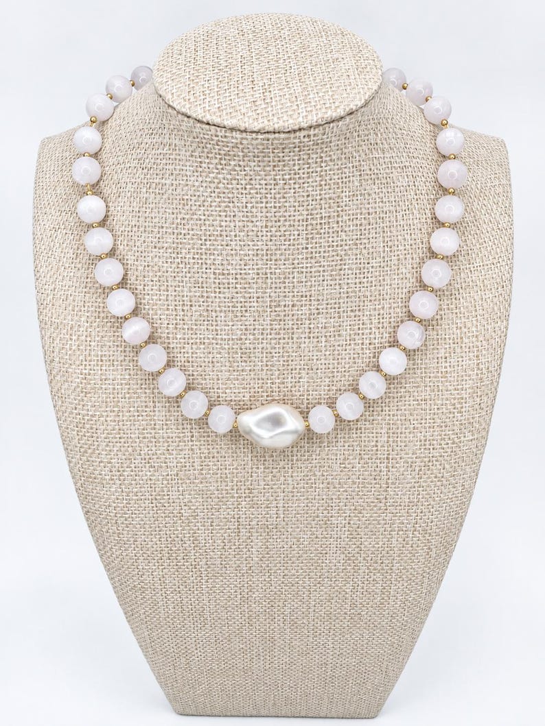 The Margaux necklace on a beige linen display bust: round pale pink gemstone beads with small gold-filled spacers and a white baroque pearl centerpiece.