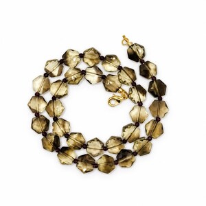 May include: A necklace featuring faceted, hexagonal smoky quartz beads in a translucent brown hue, interspersed with small, dark maroon spherical spacer beads. The strand is secured with a gold-toned metal lobster claw clasp and jump ring.