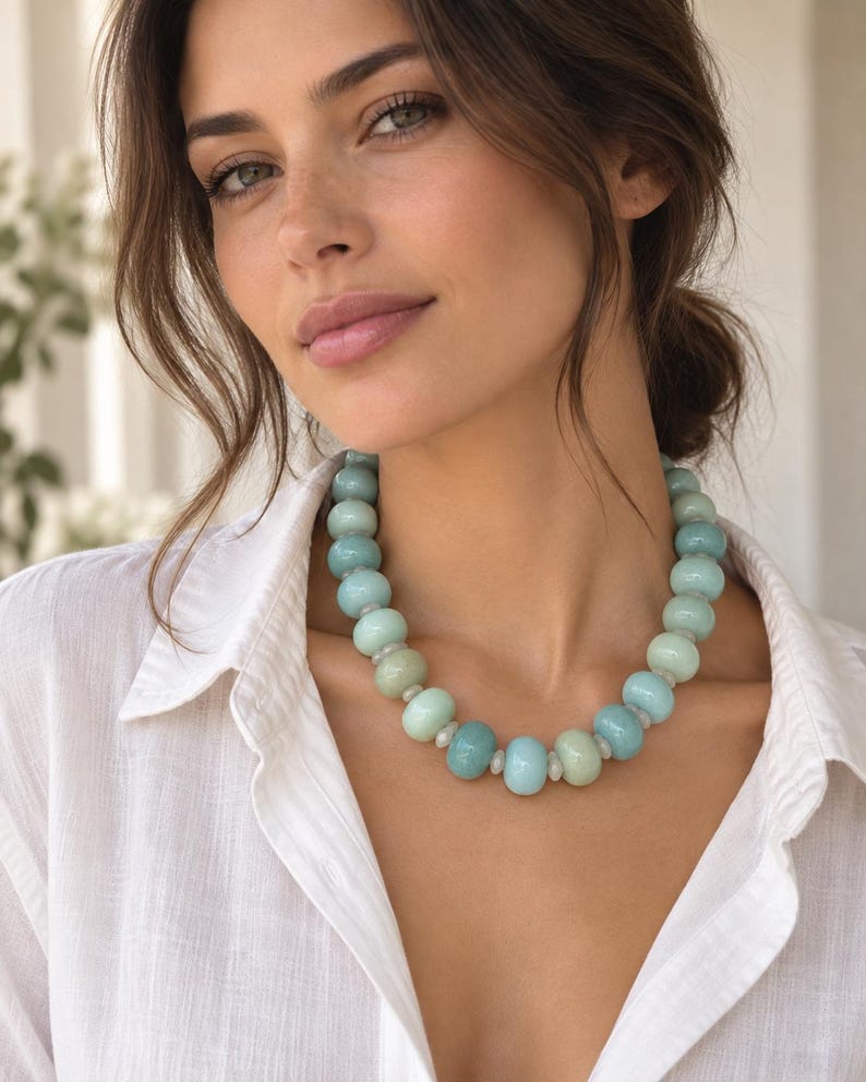 May include: A necklace featuring a series of smooth, round, light blue and pale green beads. The beads are arranged in a single strand, alternating between larger, opaque, rounded stones and smaller, translucent, clear spacers throughout the design.