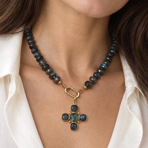 The Monaco necklace worn with an open white shirt: dark labradorite beads, a gold-colored front ring and a cross-shaped blue-green stone pendant.