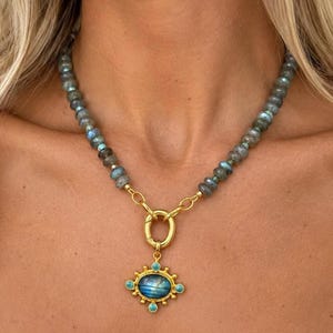 The Celeste necklace worn at the collarbone: gray labradorite beads with a gold-colored front ring and an ornate blue-green pendant.